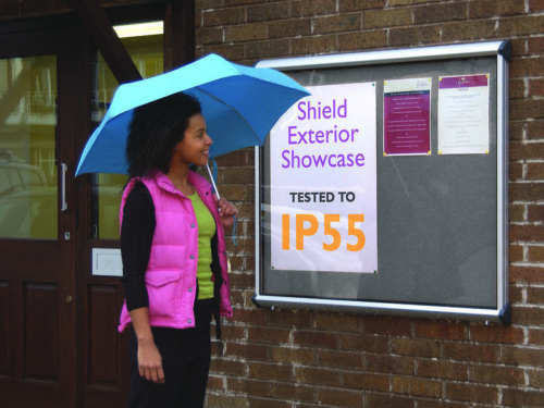 Woman walking in the rain past a Silver Framed Shield Noticeboard